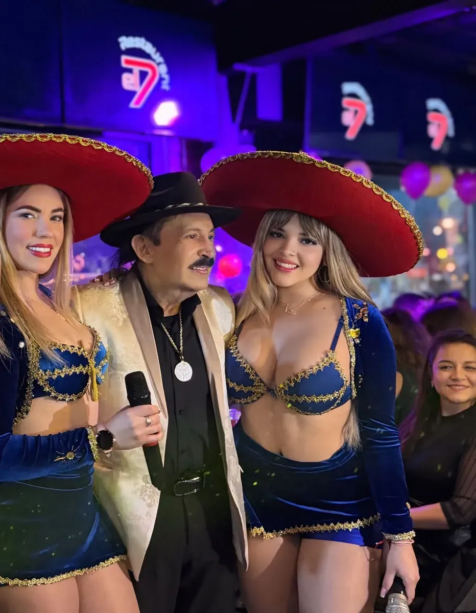 Dos integrantes de Reinas Latinas con sombreros de charro en el escenario junto a Antonio Ríos con micrófono en mano