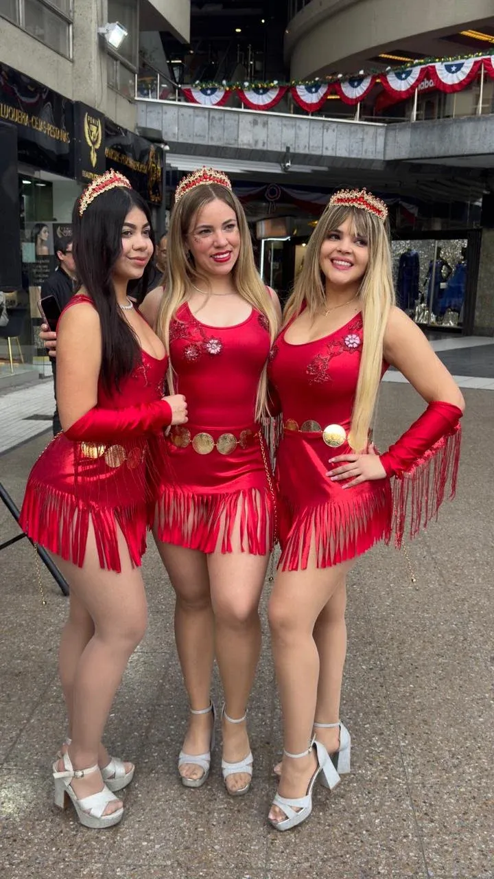 Las tres integrantes de Reinas Latinas posan juntas con trajes rojos, flecos dorados y coronas